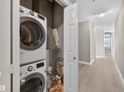 Dedicated laundry closet featuring a stacked washer and dryer, adjacent to a hallway with wood-finish flooring - 