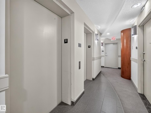 Elevator lobby featuring two elevators, recessed ceiling lighting, wall-mounted sconces, a wood-paneled column, and grey tile flooring - #1208 9939 109 St Nw, Edmonton, AB - Indoor Photo Showing Other Room
