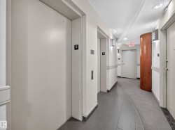Elevator lobby featuring two elevators, recessed ceiling lighting, wall-mounted sconces, a wood-paneled column, and grey tile flooring - 