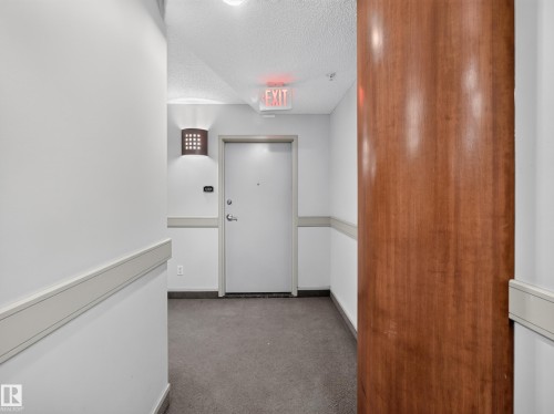 Corridor featuring light gray walls, dark gray carpet flooring, a wood-paneled column, and a modern wall sconce - #1208 9939 109 St Nw, Edmonton, AB - Indoor Photo Showing Other Room