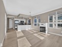 Open-concept living area featuring light wood-finish flooring, a contemporary fireplace with a decorative mantel, and a kitchen with white cabinetry and stainless steel appliances - #1208 9939 109 St Nw, Edmonton, AB  - Indoor With Fireplace 