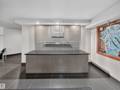 Entryway featuring a reception desk with a dark countertop, grey tile facade, and overhead recessed lighting - #1208 9939 109 St Nw, Edmonton, AB - Indoor Photo Showing Other Room