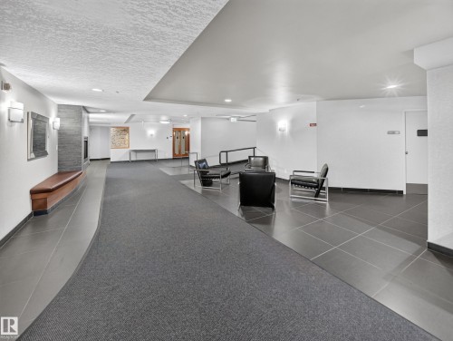 Contemporary common area featuring a carpeted walkway, large format tile flooring, wall sconces, and a built-in seating bench - #1208 9939 109 St Nw, Edmonton, AB - Indoor Photo Showing Other Room