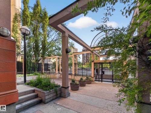 Outdoor patio space featuring a pergola structure, concrete paving, and integrated planter boxes with greenery - #1208 9939 109 St Nw, Edmonton, AB - Outdoor