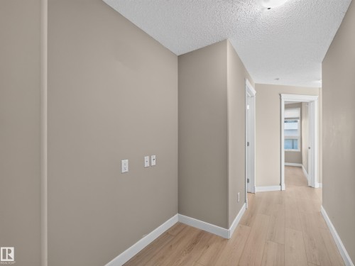 Hallway featuring light wood-finish flooring, neutral wall paint, white trim, and flush-mount ceiling lighting - #1208 9939 109 St Nw, Edmonton, AB - Indoor Photo Showing Other Room