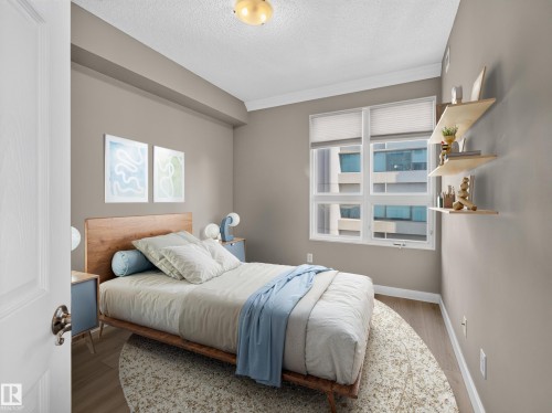 Neutral tone wall paint, wood-finish flooring, crown molding, and a multi-pane window with blinds - #1208 9939 109 St Nw, Edmonton, AB - Indoor Photo Showing Bedroom
