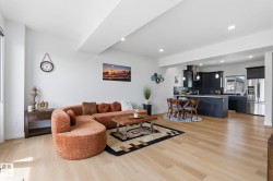 Open-concept living space featuring wood-finish flooring, recessed lighting, a modern kitchen with dark cabinetry, stainless steel appliances, and a central island - 