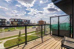 Outdoor balcony featuring wood-finish decking, black metal railings with glass panels, and a partial privacy screen - 