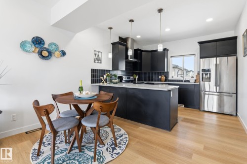 Open-concept kitchen featuring dark cabinetry, stainless steel appliances, a center island with countertop seating, and a subway tile backsplash - 8282 Chappelle Way Sw, Edmonton, AB - Indoor