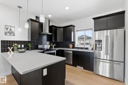 Modern kitchen featuring dark cabinetry, light countertops, stainless steel appliances, pendant lighting, and wood-finish flooring - 