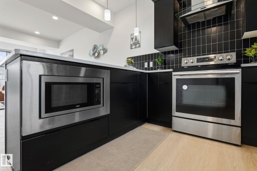 Contemporary kitchen featuring stainless steel appliances, including a built-in microwave and slide-in range, paired with black cabinetry and subway tile backsplash - 8282 Chappelle Way Sw, Edmonton, AB - Indoor Photo Showing Kitchen With Stainless Steel Kitchen