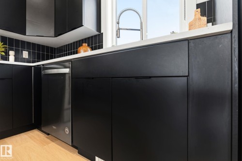 Contemporary kitchen featuring sleek black cabinetry, a stainless steel dishwasher, a white countertop, a black tile backsplash, and a gooseneck faucet - 8282 Chappelle Way Sw, Edmonton, AB - Indoor