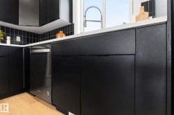 Contemporary kitchen featuring sleek black cabinetry, a stainless steel dishwasher, a white countertop, a black tile backsplash, and a gooseneck faucet - 