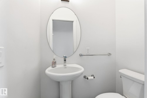 Pedestal sink with chrome faucet, oval wall mirror, and modern wall sconce - 8282 Chappelle Way Sw, Edmonton, AB - Indoor Photo Showing Bathroom