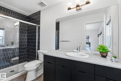 Bathroom featuring a walk-in shower with black subway tile, a single vanity with a white countertop, dark cabinetry, and a large wall-mounted mirror - 8282 Chappelle Way Sw, Edmonton, AB - Indoor Photo Showing Bathroom