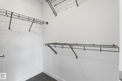 Walk-in closet featuring white walls, dark wire shelving, and dark textured carpeting - 