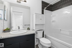 Bathroom featuring a dark vanity with integrated sink, a light-toned countertop, a frameless wall mirror, and a built-in tub with dark subway tile surround - 