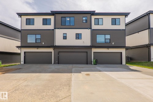 Modern townhome exterior featuring a multi-story design, horizontal siding in contrasting tones, dark-framed windows, and three integrated garages with dark doors - 8282 Chappelle Way Sw, Edmonton, AB - Outdoor With Facade