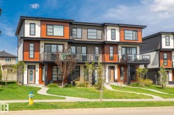 Contemporary townhome facade featuring wood-look siding, white and dark grey accents, expansive windows, and a glass-paneled balcony - 