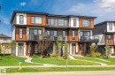 Contemporary townhome facade featuring wood-look siding, white and dark grey accents, expansive windows, and a glass-paneled balcony - 8282 Chappelle Way Sw, Edmonton, AB  - Outdoor With Facade 
