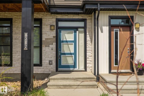 Modern exterior featuring a teal entry door with frosted glass panels, light-toned stone veneer siding, and a dark vertical structural beam - 8282 Chappelle Way Sw, Edmonton, AB - Outdoor