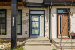 Modern exterior featuring a teal entry door with frosted glass panels, light-toned stone veneer siding, and a dark vertical structural beam - 