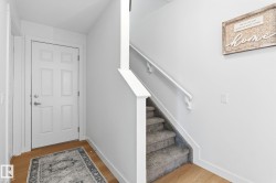 Entryway featuring light wood-finish flooring, a paneled door, and a staircase with carpeted treads and a white handrail - 