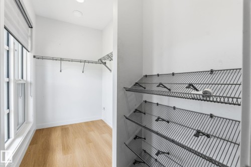 Walk-in closet with wood-finish flooring, a window with roller shade, overhead lighting, and wire shelving - 8282 Chappelle Way Sw, Edmonton, AB - Indoor