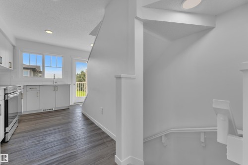 Kitchen featuring wood-finish flooring, white cabinetry with gold-tone hardware, white subway tile backsplash, stainless steel range, and a glass-paned door leading to an outdoor space - #64 17832 78 St Nw Nw, Edmonton, AB - Indoor Photo Showing Other Room