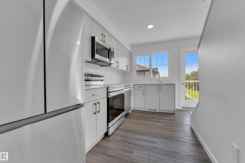 Modern kitchen featuring white cabinetry, stainless steel appliances, wood-finish flooring, recessed lighting, and a walk-out to an exterior balcony - #64 17832 78 St Nw Nw, Edmonton, AB - Indoor Photo Showing Kitchen