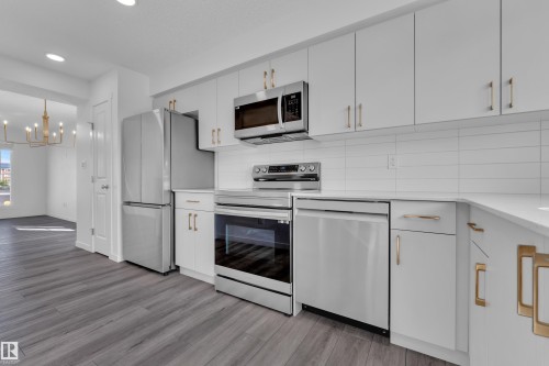 Modern kitchen featuring stainless steel appliances, white cabinetry with gold-tone hardware, white subway tile backsplash, and wood-finish flooring - #64 17832 78 St Nw Nw, Edmonton, AB - Indoor Photo Showing Kitchen
