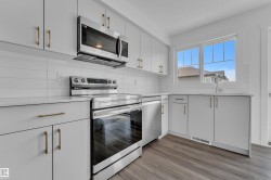 Modern kitchen featuring light gray cabinetry with gold-finish hardware, stainless steel appliances, white subway tile backsplash, and wood-finish flooring - 