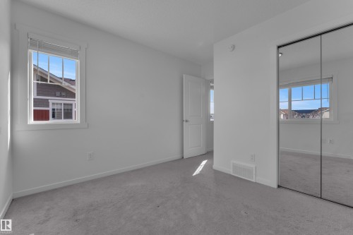 Carpeted room featuring a white interior door, a window with white trim, and a mirrored closet - #64 17832 78 St Nw Nw, Edmonton, AB - Indoor Photo Showing Other Room
