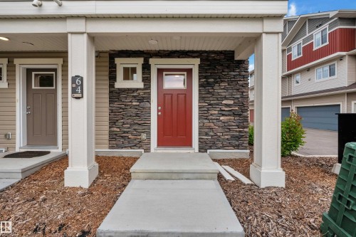 Inviting front entry featuring a bold red door, stacked stone facade, and a covered porch with white columns - #64 17832 78 St Nw Nw, Edmonton, AB - Outdoor