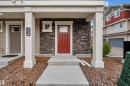 Inviting front entry featuring a bold red door, stacked stone facade, and a covered porch with white columns - #64 17832 78 St Nw Nw, Edmonton, AB  - Outdoor 