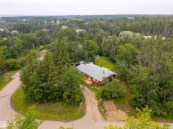 Ranch-style residence nestled in a wooded setting, featuring a gray shingle roof and a red siding exterior - 