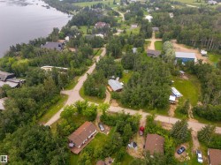Aerial perspective showcasing a residential area featuring multiple homes, mature trees, unpaved roads, and a prominent waterfront bordering the property - 