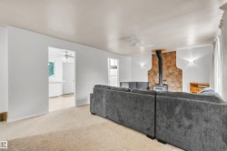 Living area featuring a stone accent wall with a wood-burning stove, ceiling fan, carpet flooring, and sconce lighting - 