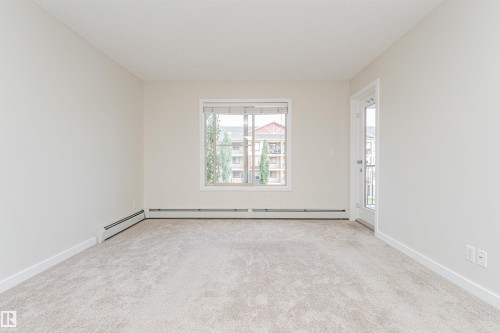 Spacious room featuring light-toned carpet, neutral wall paint, and white trim - #322 5816 Mullen Pl Nw, Edmonton, AB - Indoor Photo Showing Other Room