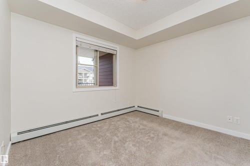 Carpeted room featuring a window with horizontal blinds, baseboard heating, and ceiling trim - #322 5816 Mullen Pl Nw, Edmonton, AB - Indoor Photo Showing Other Room
