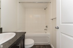 Bathroom featuring a built-in bathtub with white tile surround, dark wood-finish vanity with an integrated sink, and dark tile flooring - 