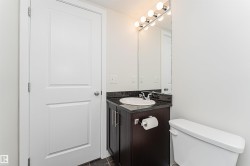 Bathroom featuring a dark wood-finish vanity, a black countertop, a white ceramic sink, and a mirrored vanity light fixture - 