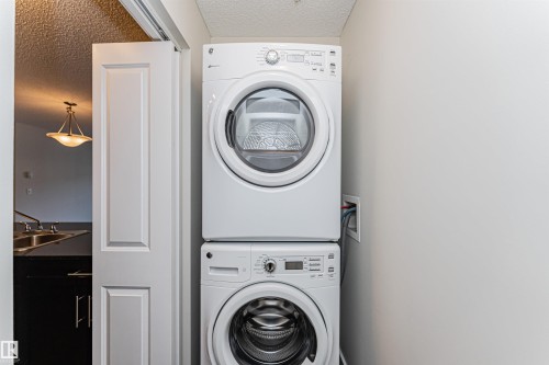 Stackable washer and dryer unit, featuring white finishes and digital controls - #322 5816 Mullen Pl Nw, Edmonton, AB - Indoor Photo Showing Laundry Room
