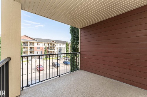 Outdoor balcony featuring a textured concrete floor, a black metal railing, and a wood-paneled exterior wall - #322 5816 Mullen Pl Nw, Edmonton, AB - Outdoor With Exterior