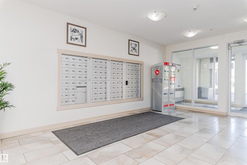 Lobby area featuring light-toned tile flooring, recessed wall-mounted mailboxes, and glass entry doors - #322 5816 Mullen Pl Nw, Edmonton, AB - Indoor Photo Showing Other Room