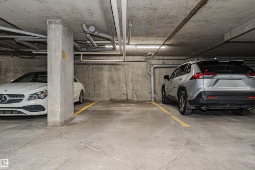 Dedicated parking space within a subterranean garage, featuring concrete flooring, concrete walls, and overhead lighting - #322 5816 Mullen Pl Nw, Edmonton, AB - Indoor Photo Showing Garage