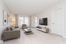 Spacious living area featuring light-toned carpeting, a large window with drapes, and a white interior door - #322 5816 Mullen Pl Nw, Edmonton, AB  - Indoor Photo Showing Living Room 