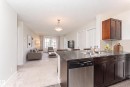 Kitchen island with granite-style countertop and stainless-steel dishwasher - #322 5816 Mullen Pl Nw, Edmonton, AB  - Indoor Photo Showing Kitchen With Double Sink 