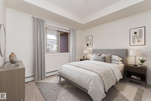 Bedroom featuring light-colored walls, a tray ceiling, and a large window with blinds and drapes - #322 5816 Mullen Pl Nw, Edmonton, AB - Indoor Photo Showing Bedroom
