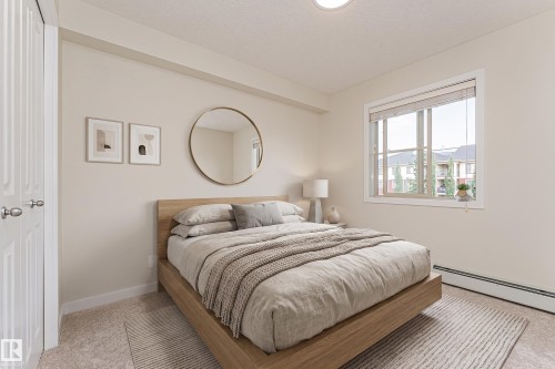 Spacious bedroom featuring light neutral wall tones, plush carpet flooring, a large window with blinds, and white trim - #322 5816 Mullen Pl Nw, Edmonton, AB - Indoor Photo Showing Bedroom